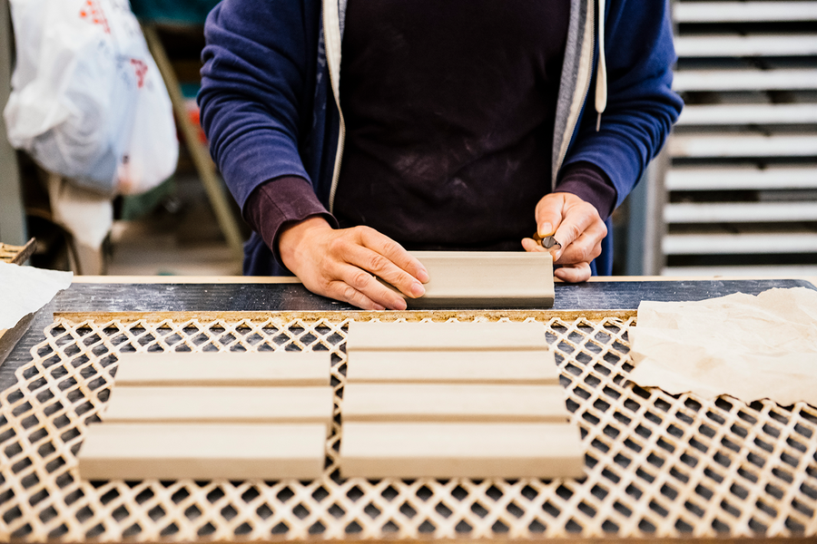 A Pewabic artisan is trimming rectangular clay pieces that will eventually become tiles in an architectural installation.