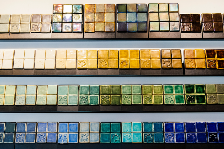 The tile sample wall in our tile showroom displays 3x3 square tile boards in bright blue, green and yellow glazes.