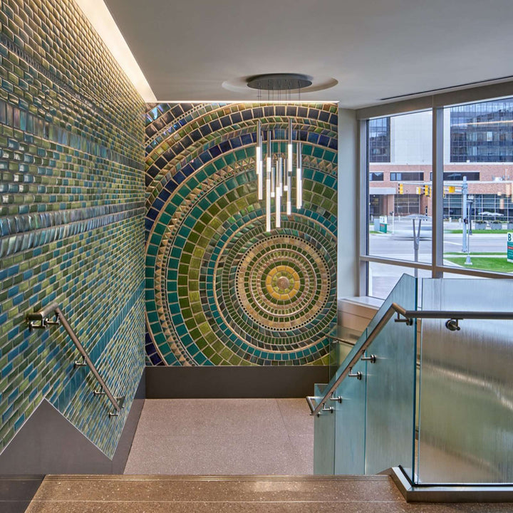 A large scale mural of concentric circles in yellows, greens, and blues line the walls of a wide, modern staircase.