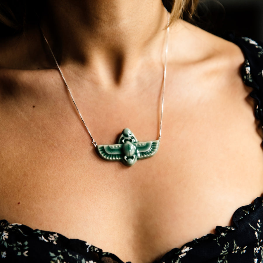 This high relief ceramic necklace features a stylized scarab with outstretched wings. The ends of each wing are attached to the silver chain.