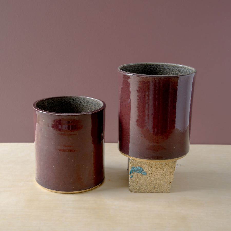 Merlot is a rich, muted, burgundy glaze born from a misfiring of our seasonal Winterberry glaze. Two Pewabic Crocks are displayed on a natural wood foreground and mauve background.