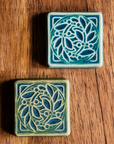 The DIA Leaf and Berries tile features two intertwined branches with round berries that create a circle at the center of the tile. The thick lined border makes the tile into a square. This tile is in the Lime/Lagoon color palette. 