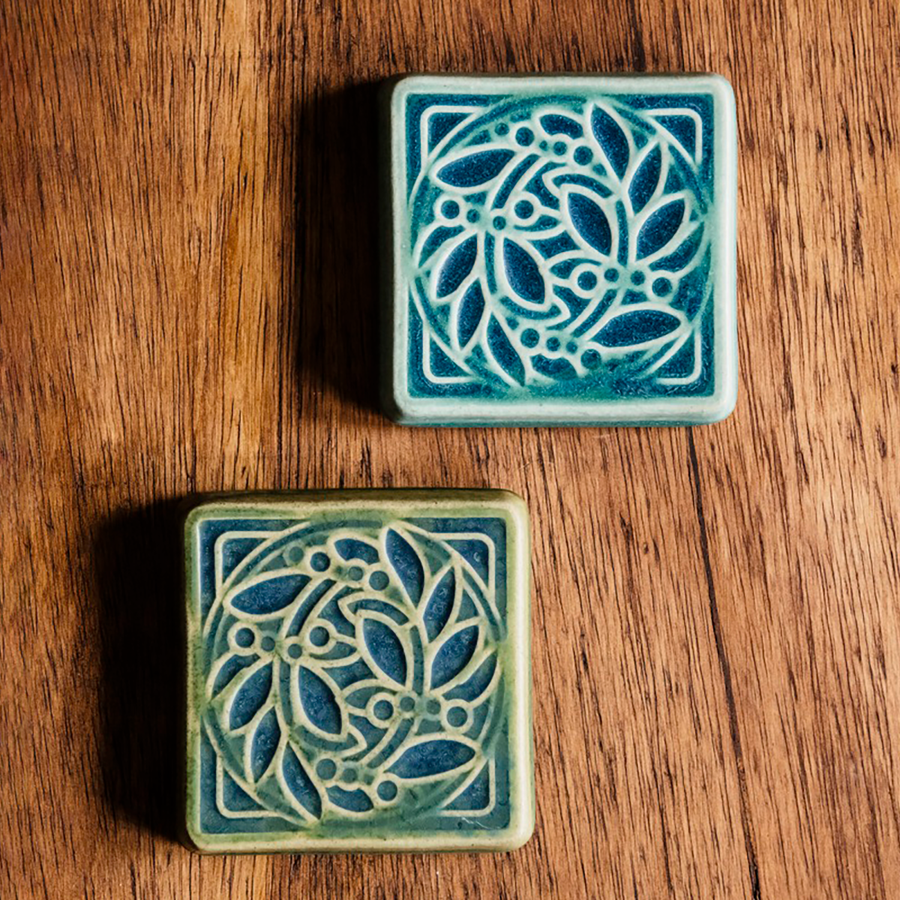 The DIA Leaf and Berries tile features two intertwined branches with round berries that create a circle at the center of the tile. The thick lined border makes the tile into a square. This tile is in the Lime/Lagoon color palette. 