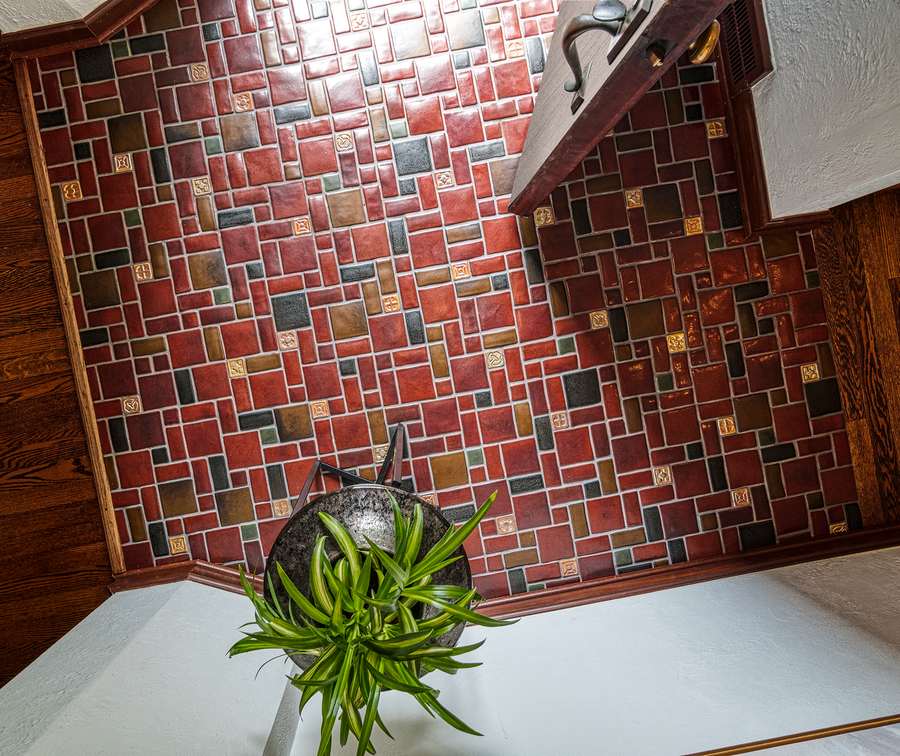 An aerial view of a foyer floor made of rust and gold colored Pewabic tiles in a pattern of square and rectangular shapes.