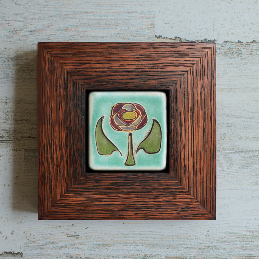 The Hand-Painted Rose Tile features a line drawing of a pinkish dusty rose in the center with a green stem and leaves on a pale blue background. The frame is a deep reddish brown oak wood frame.