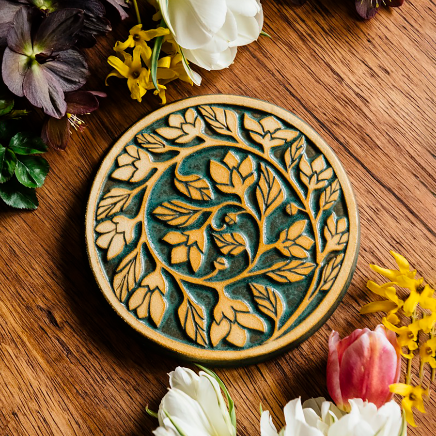 The round Ivy Trivet features a long branch of leafy ivy that curves into a spiral that ends in the center of the trivet. 