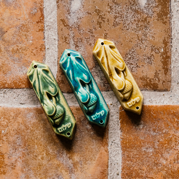 This ceramic Mezuzah features an acorn and oak leaf with the word "Peace" written in Hebrew below them. This piece is thick with an opening on the back to hold your written prayer. There are two holes at the top and bottom to make it easy to attach to your doorframe.