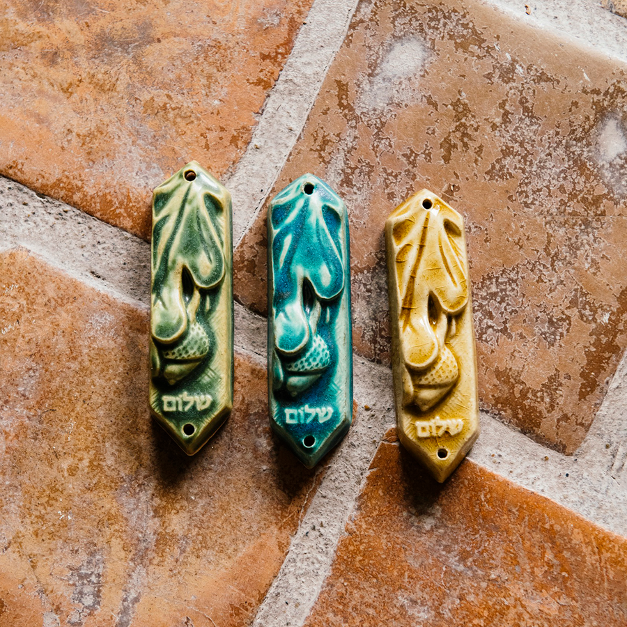 This ceramic Mezuzah features an acorn and oak leaf with the word "Peace" written in Hebrew below them. This piece is thick with an opening on the back to hold your written prayer. There are two holes at the top and bottom to make it easy to attach to your doorframe.