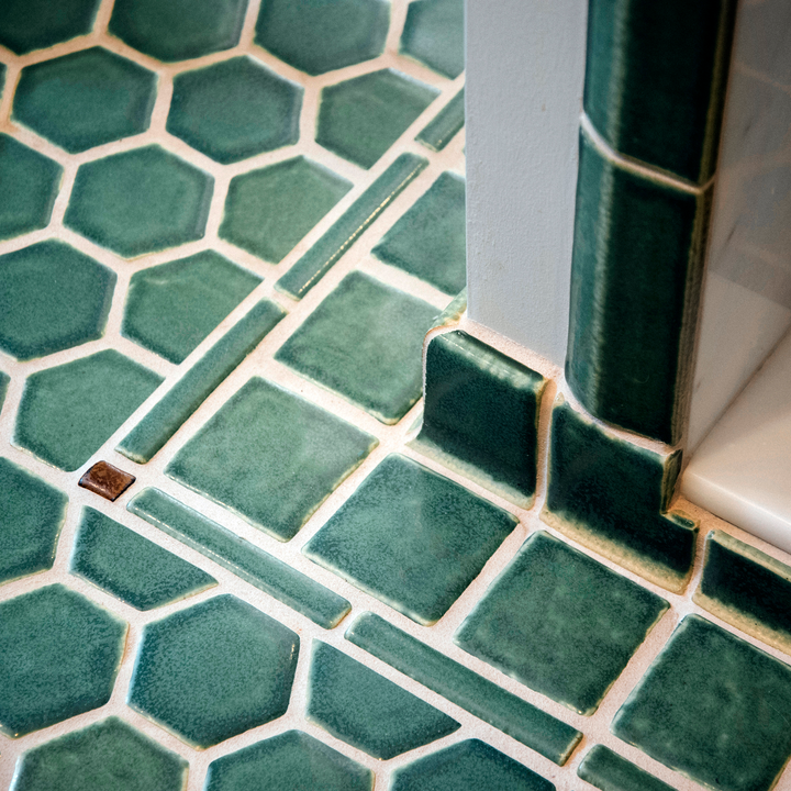 A bathroom floor is made of green Pewaibc tiles in many decorative shapes including squares, hexagons, and long rectangular borders.