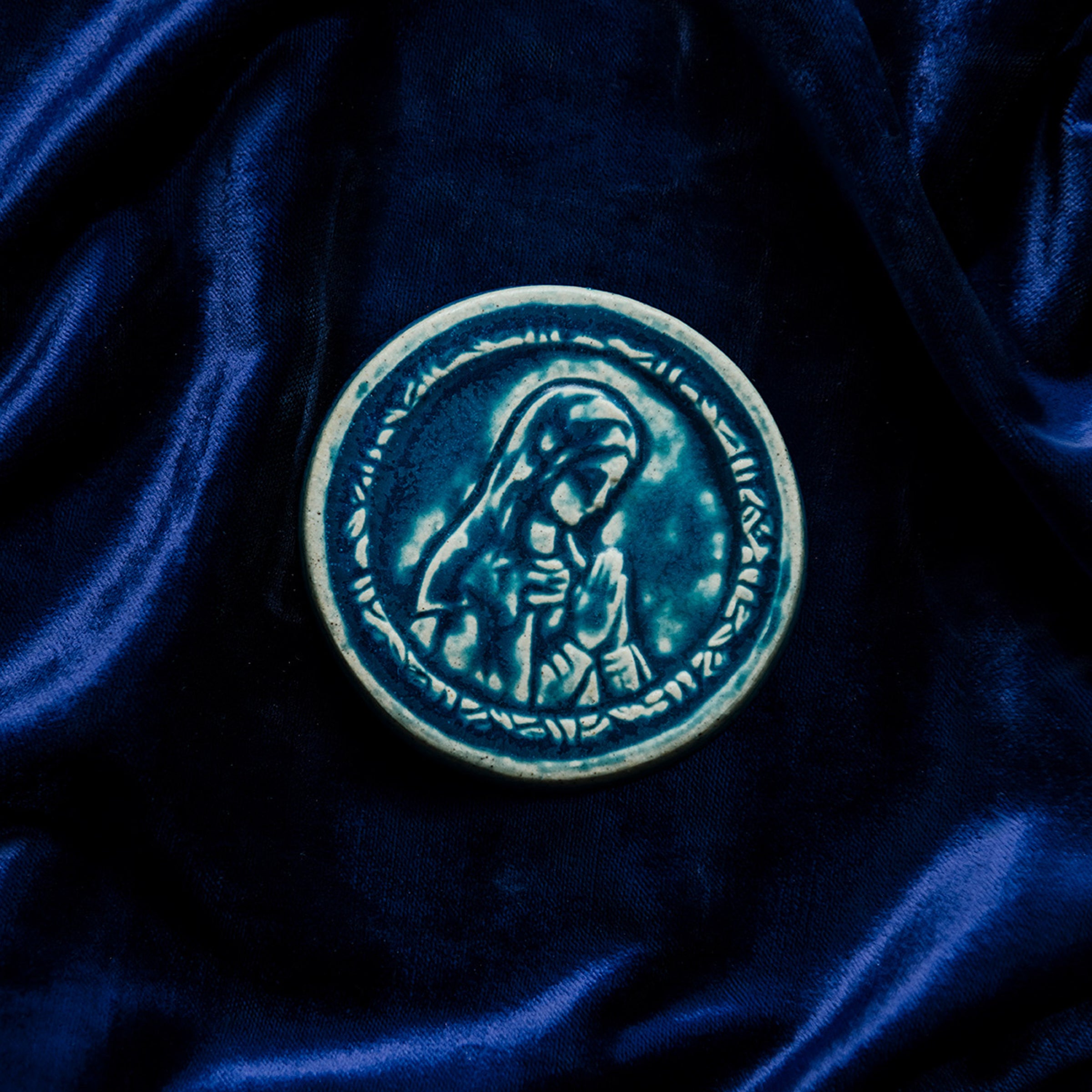 This ceramic Blessed Virgin Mary Tile is glazed in a French-blue, matte Peacock glaze resting on a bed of rich, blue velvet.