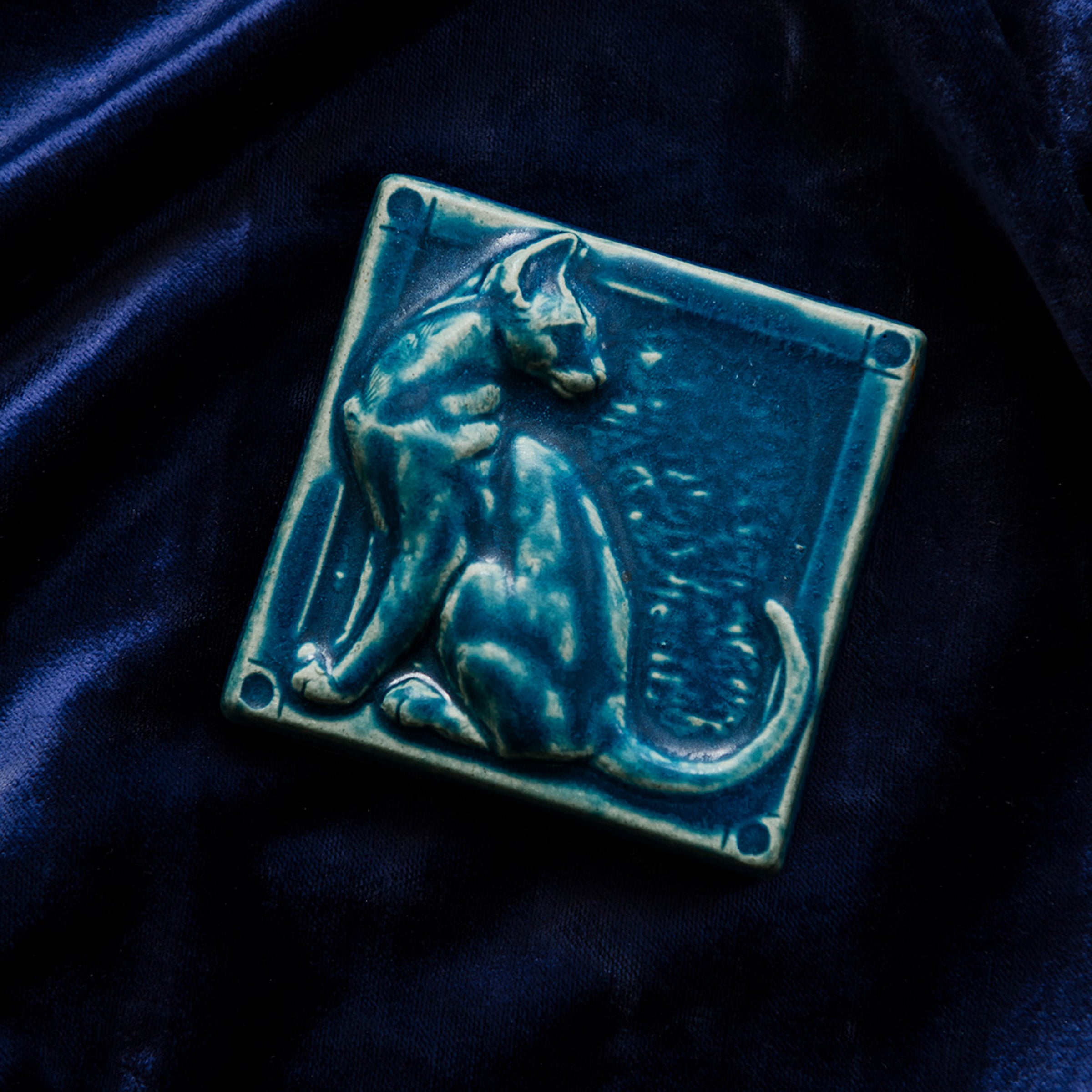 This cat tile is shown in a matte-blue Peacock glaze resting on a bed of rich, blue velvet. 