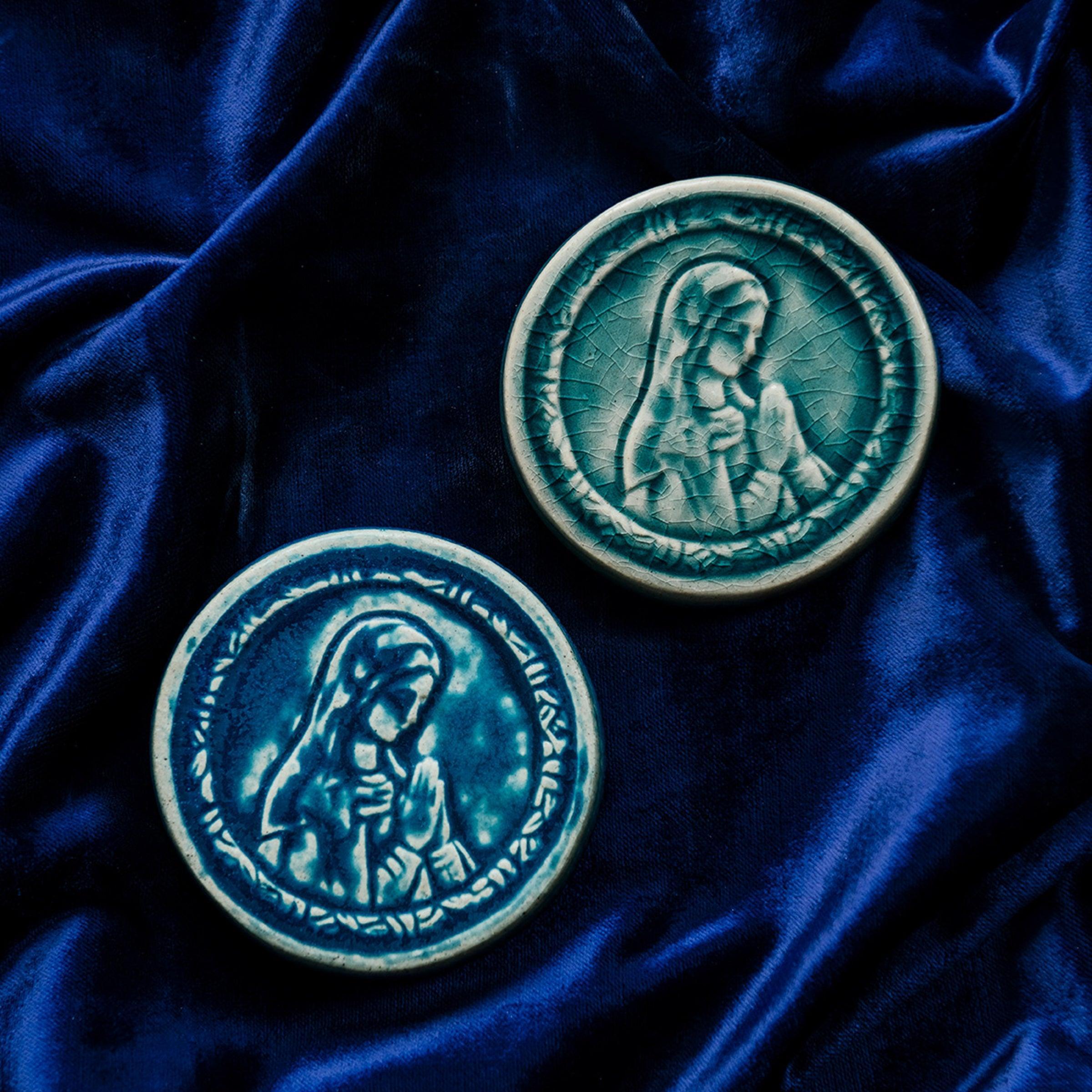 These ceramic Blessed Virgin Mary Tile are glazed in a pale blue, glossy Glacier glaze and French-blue Peacock glaze. They are resting on a bed of rich, blue velvet.