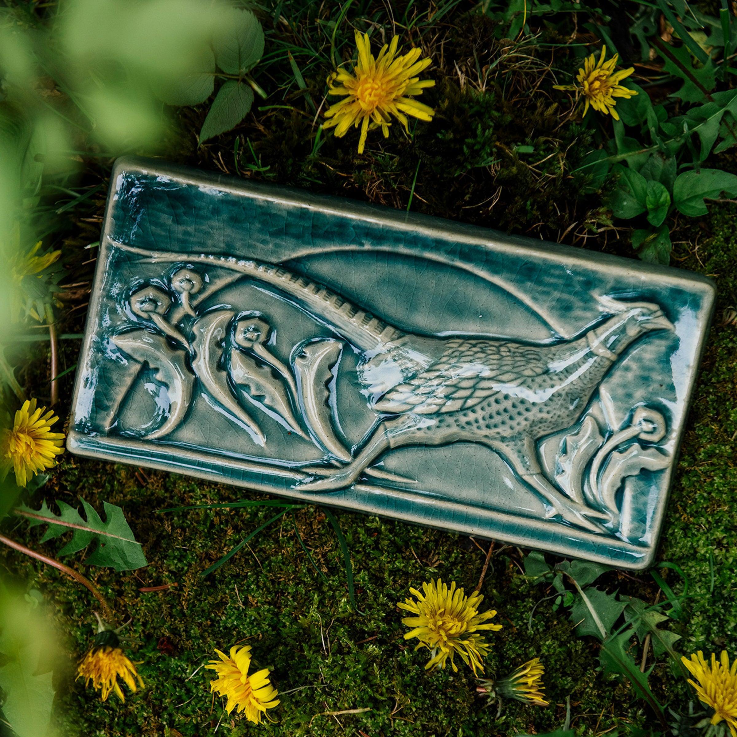 This hand-sculpted tile features a pheasant running through a field of dandelions. It is featured in a glossy blue Glacier glaze. 