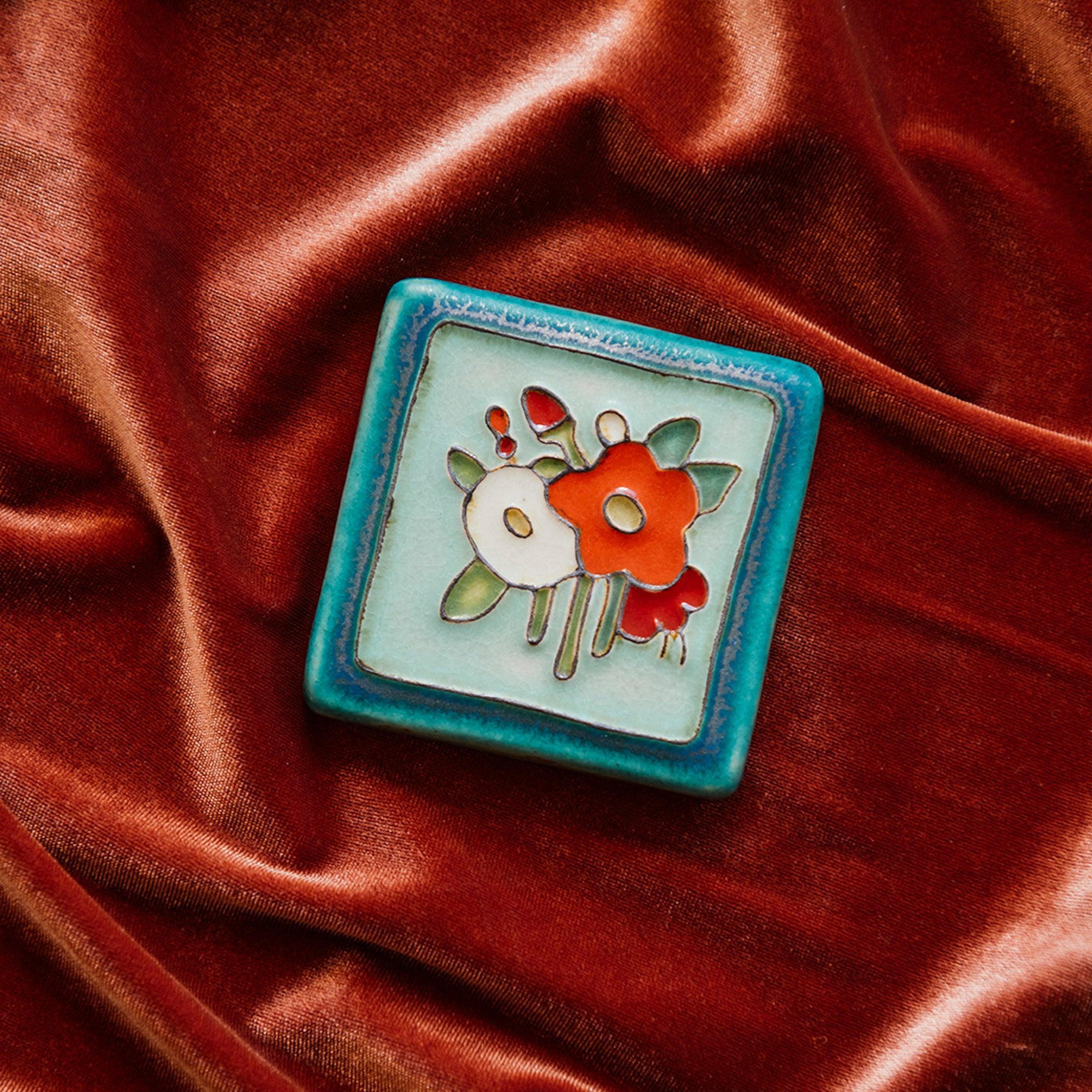 A Hand-Painted Bouquet Tile in our "Poppy Palette" rests on a bed of rich, organge-pink velvet. 