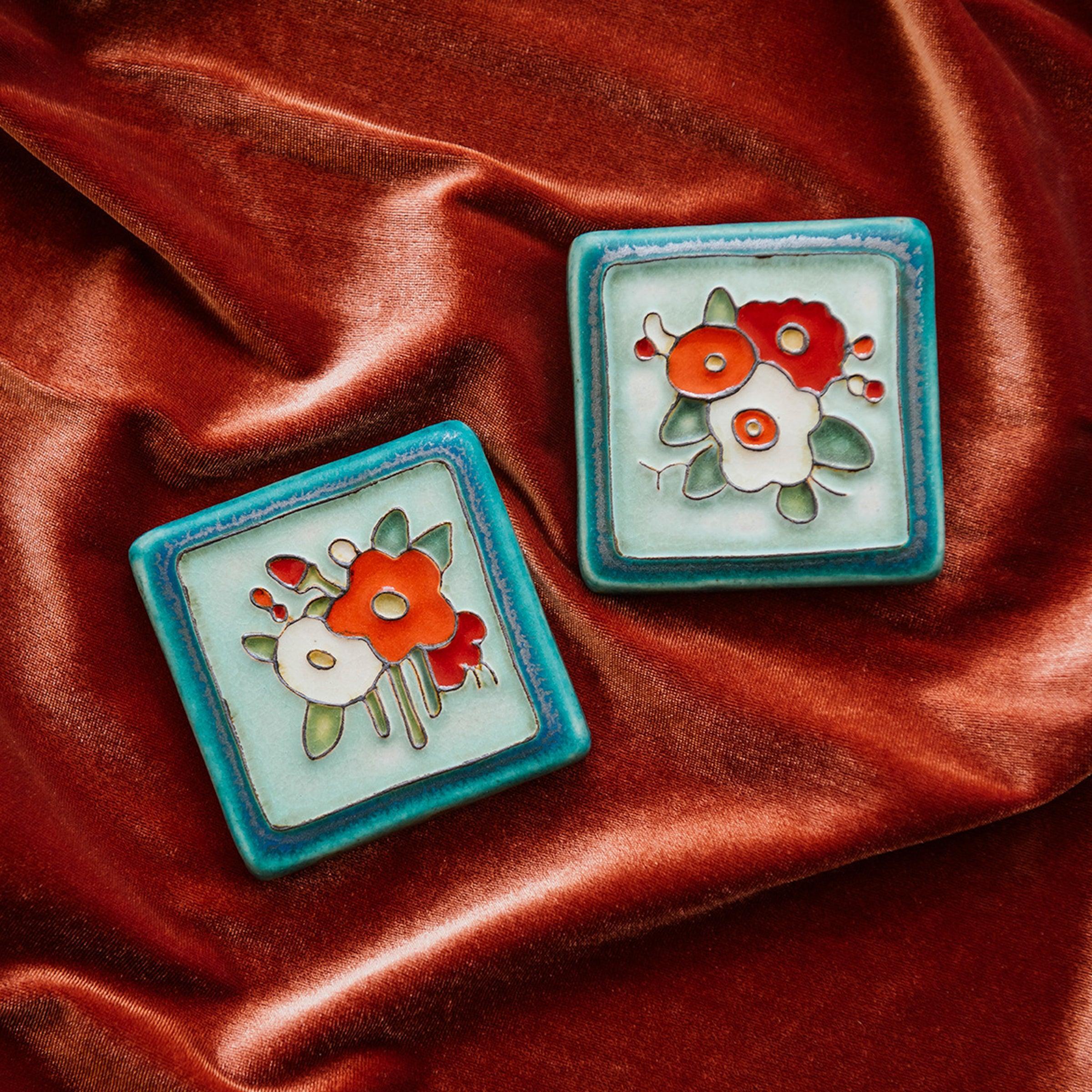 A Hand-Painted Three Flowers Tile and Hand-Painted Bouquet Tile both in our "Poppy Palette" rests on a bed of rich, organge-pink velvet. 