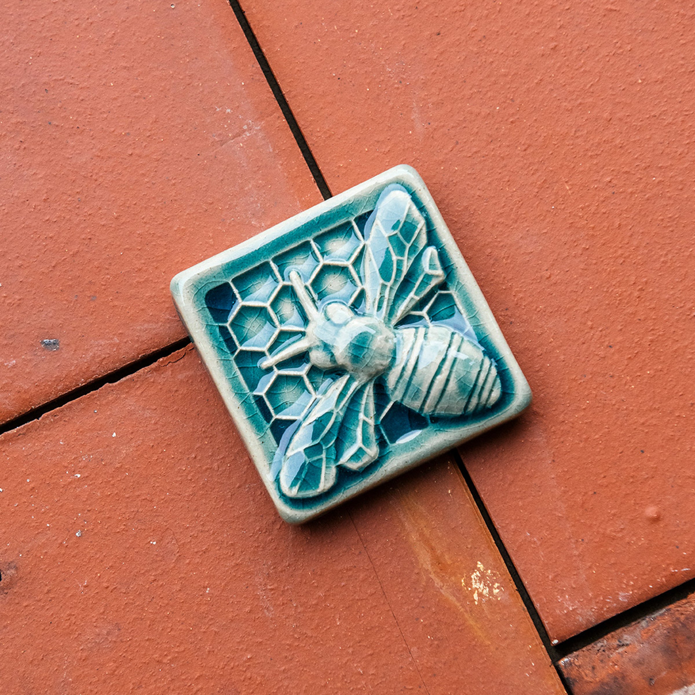 A glossy blue bee tile rests on deep terracotta colored roof tiles. 