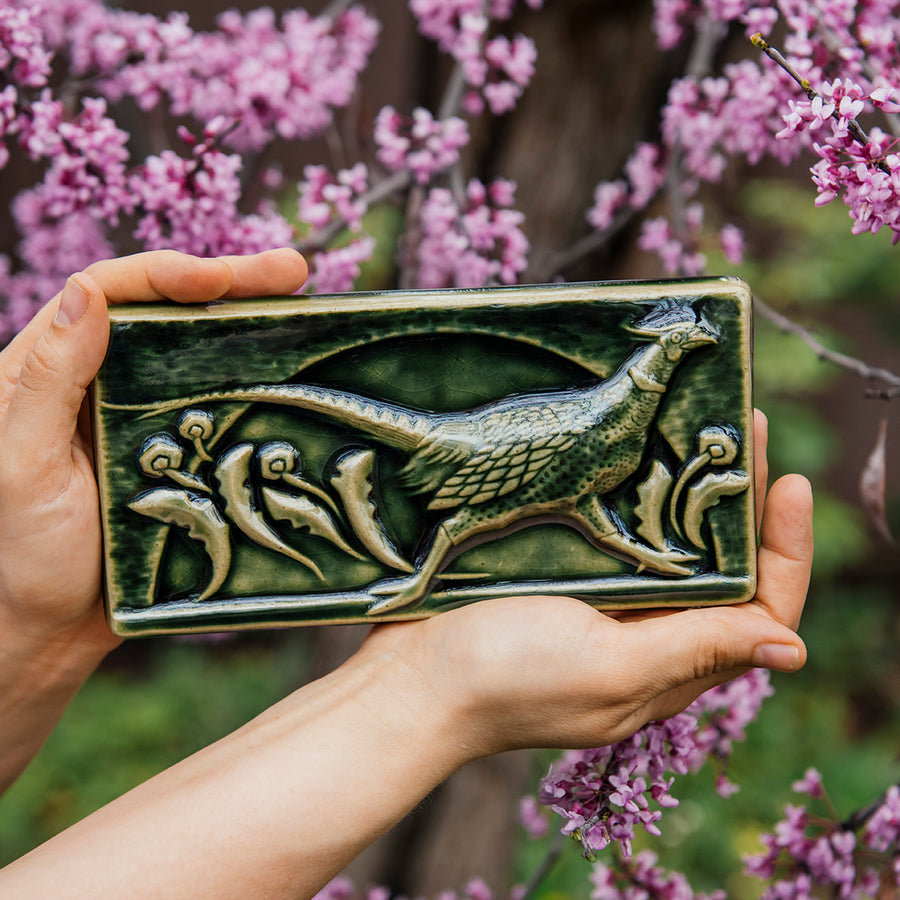 This hand-sculpted tile features a pheasant running through a field of dandelions. It is featured in a glossy green Kale glaze. 