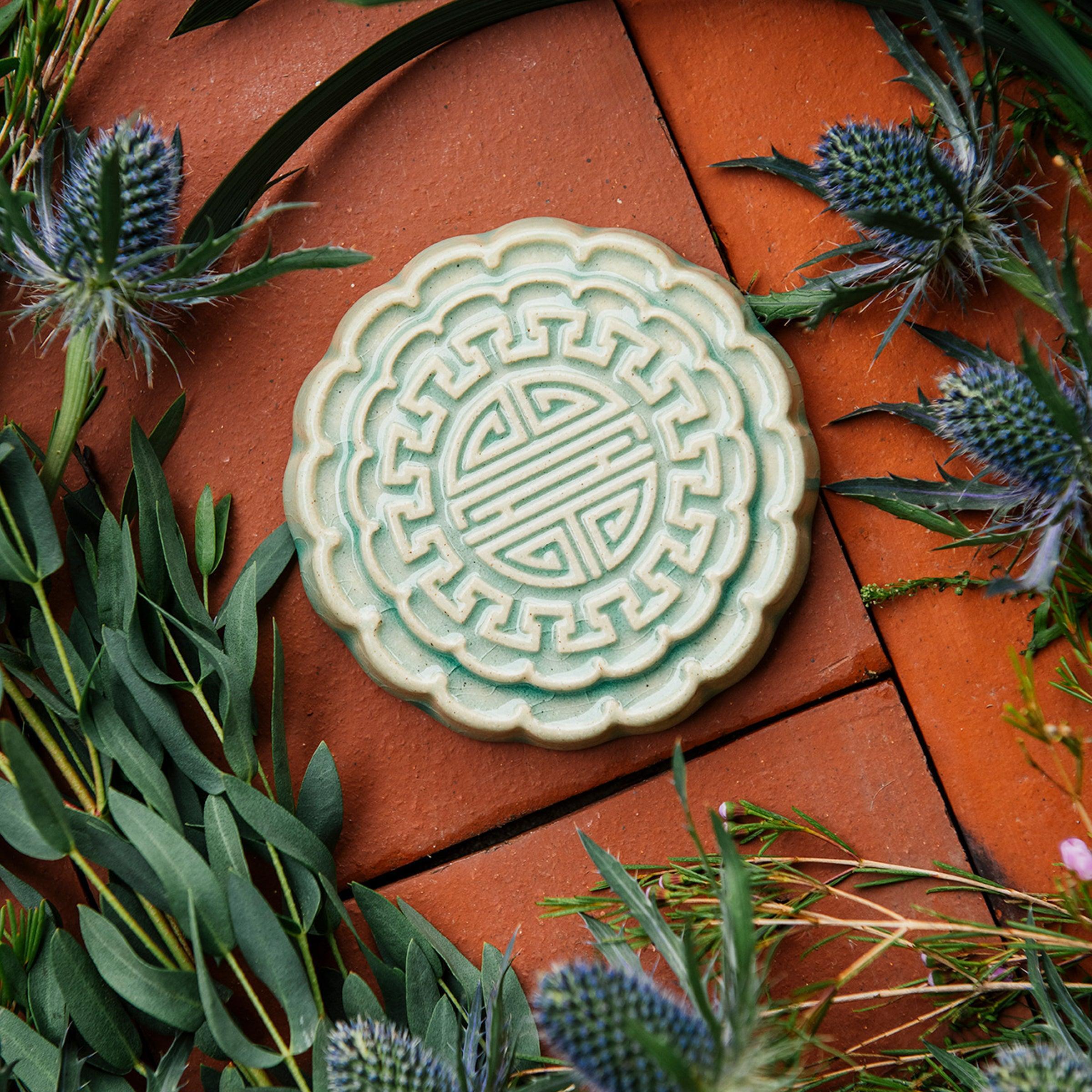 A Mooncake Paperweight in our glossy Celadon glaze, surrounded by thistle and wax flowers. 