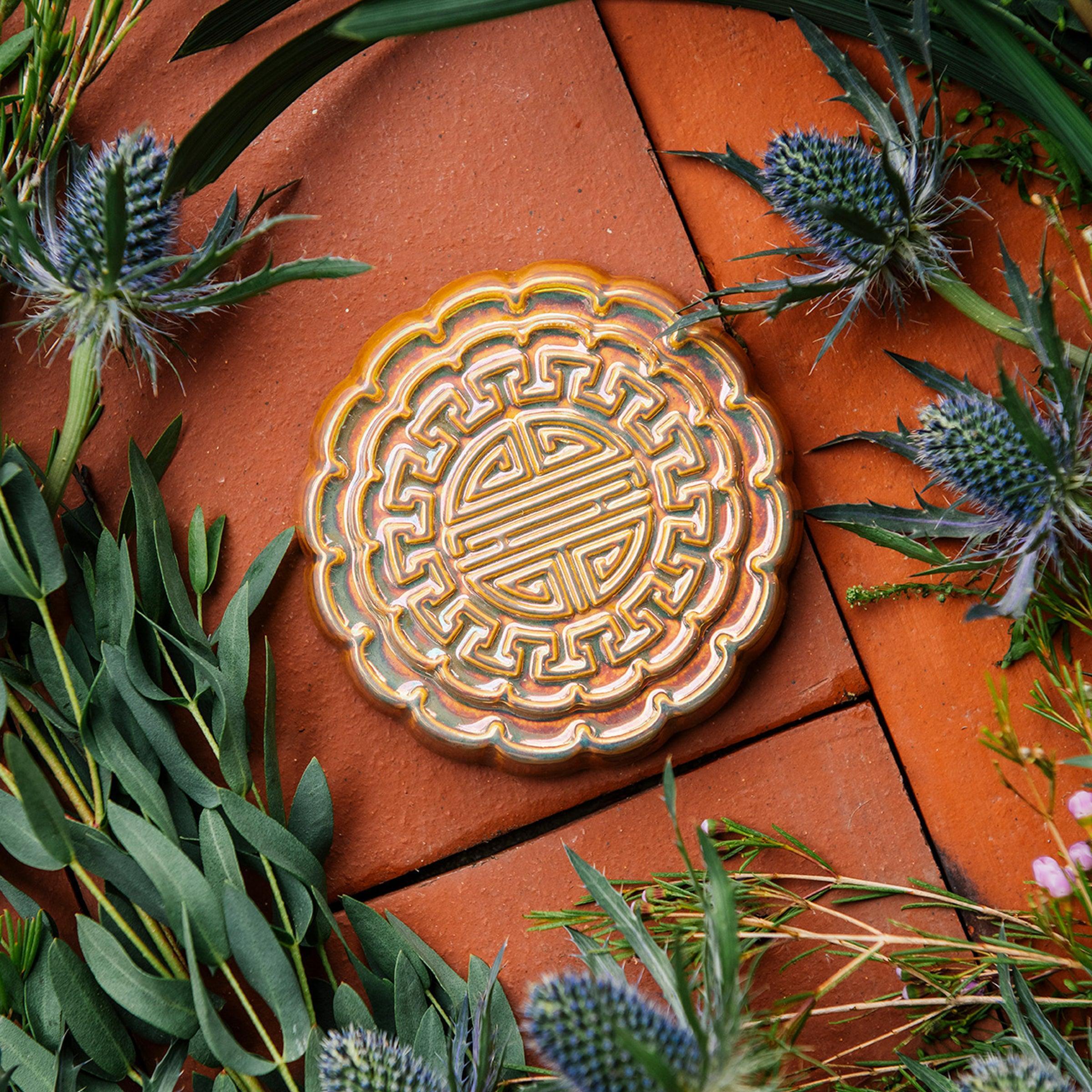 A Mooncake Paperweight in shimmering Blush Iridescent surrounded by thistle and wax flowers. 