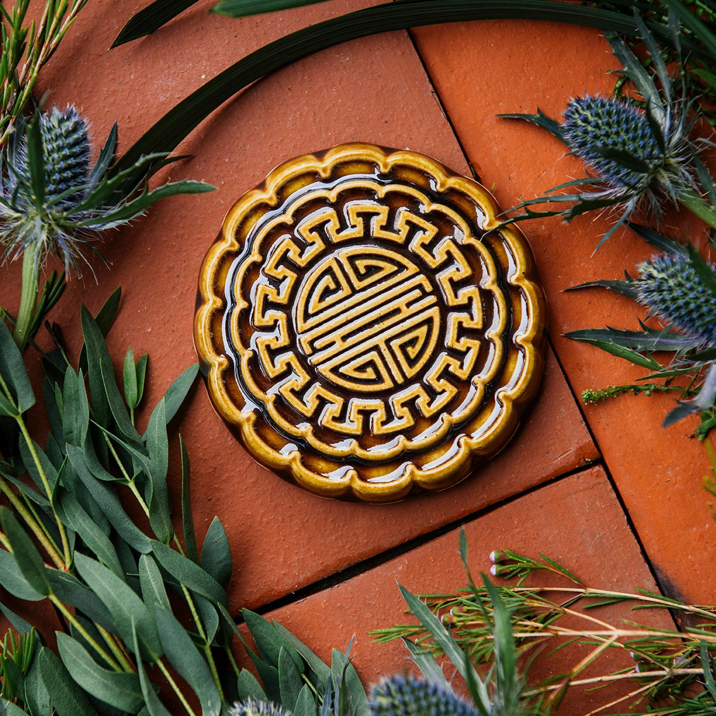 A Mooncake Paperweight in our glossy Molasses glaze, surrounded by thistle and wax flowers. 