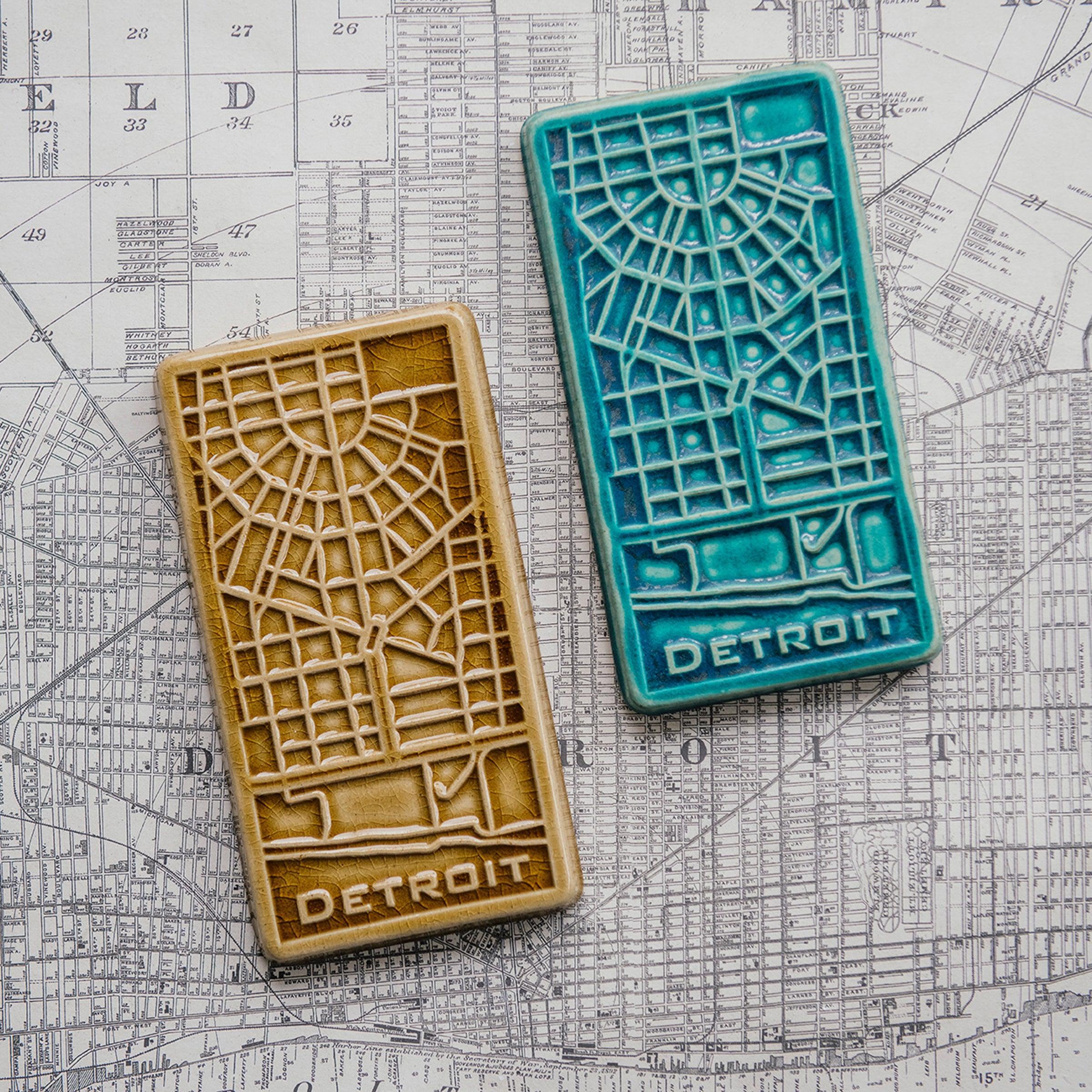 The Pewabic Blue and Honey glazed tiles lay next to each other on a black and white street map of Detroit. 