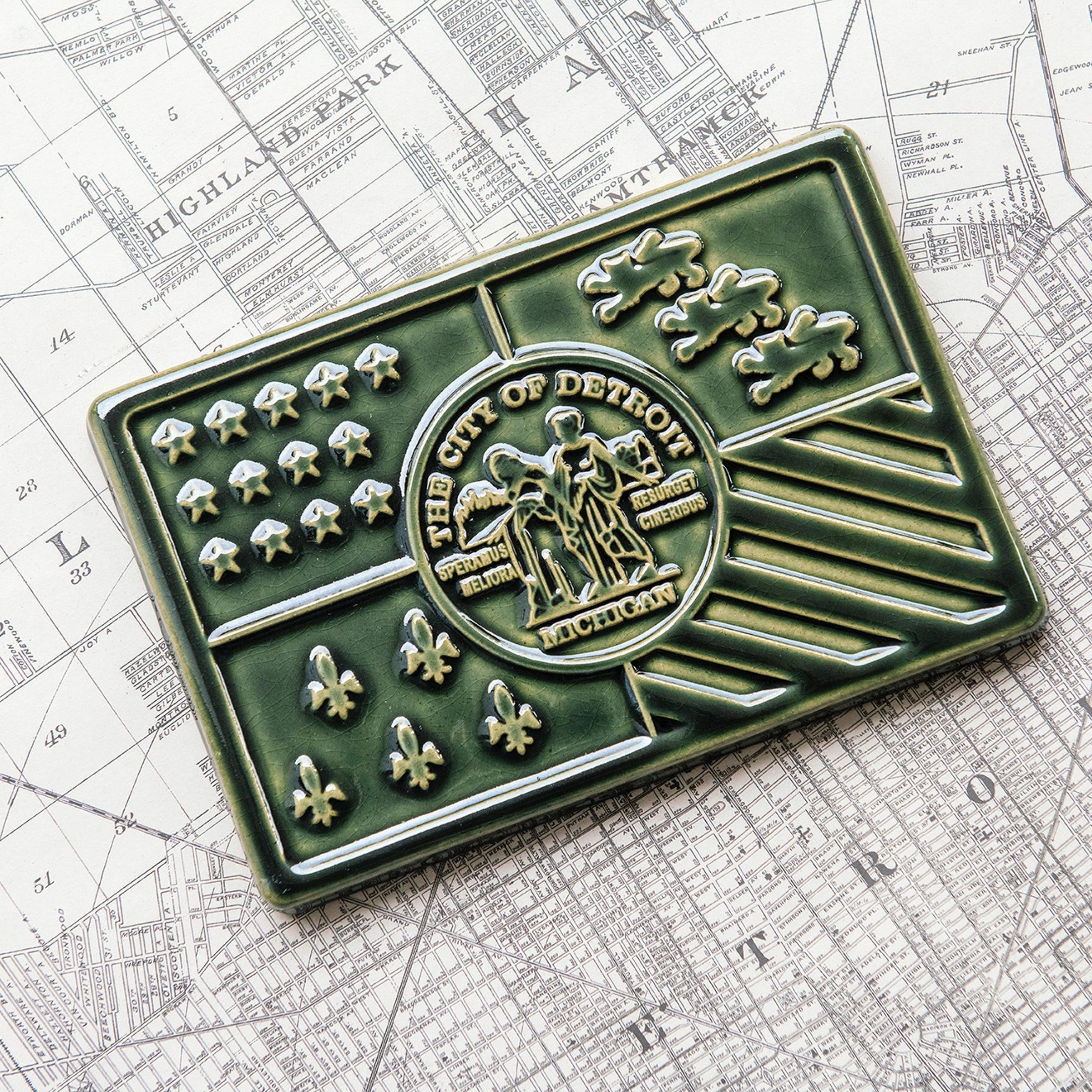 A Kale Detroit Flag Tile sits on a black and white street map of Detroit. 