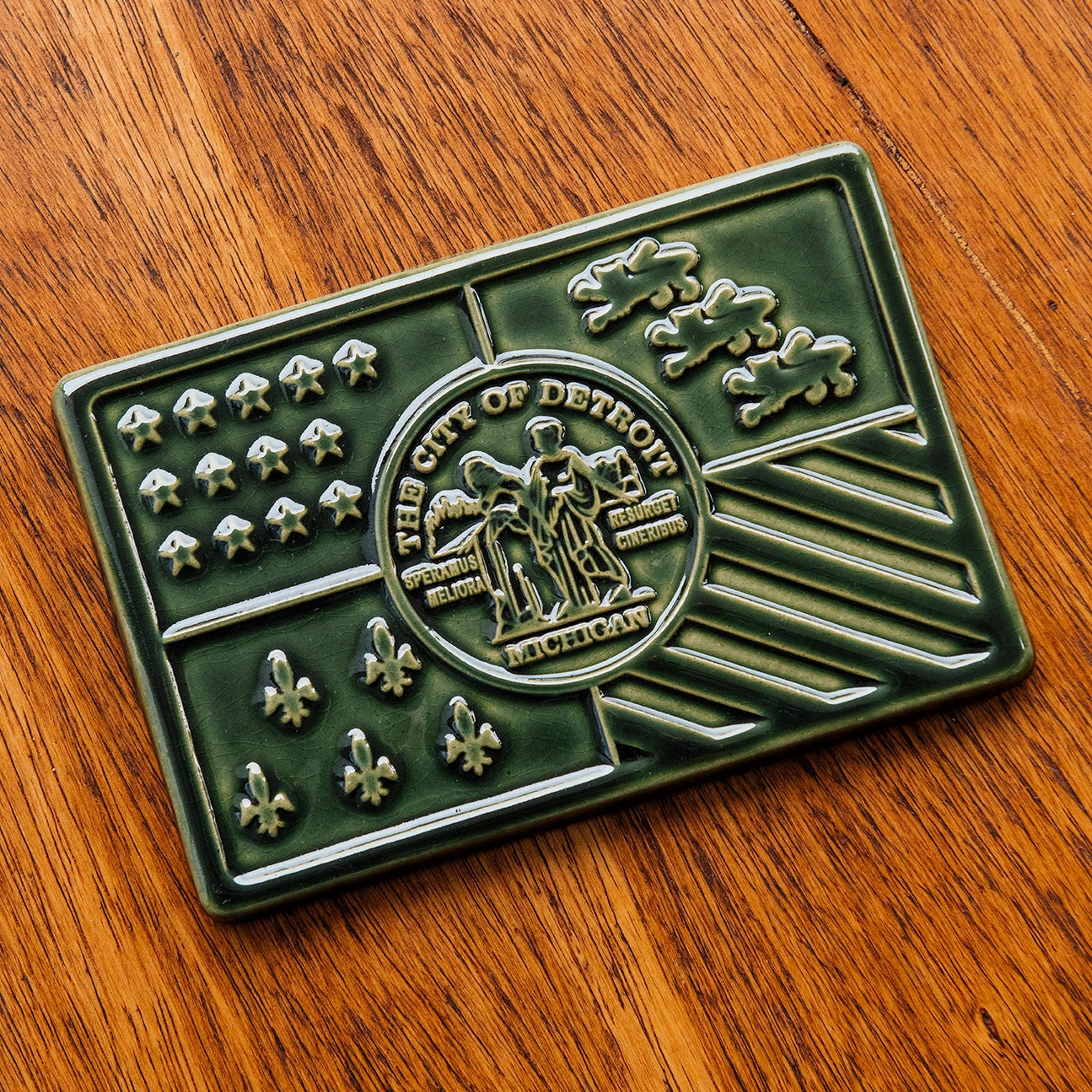 A Kale Detroit Flag tile rests on a wooden table. 