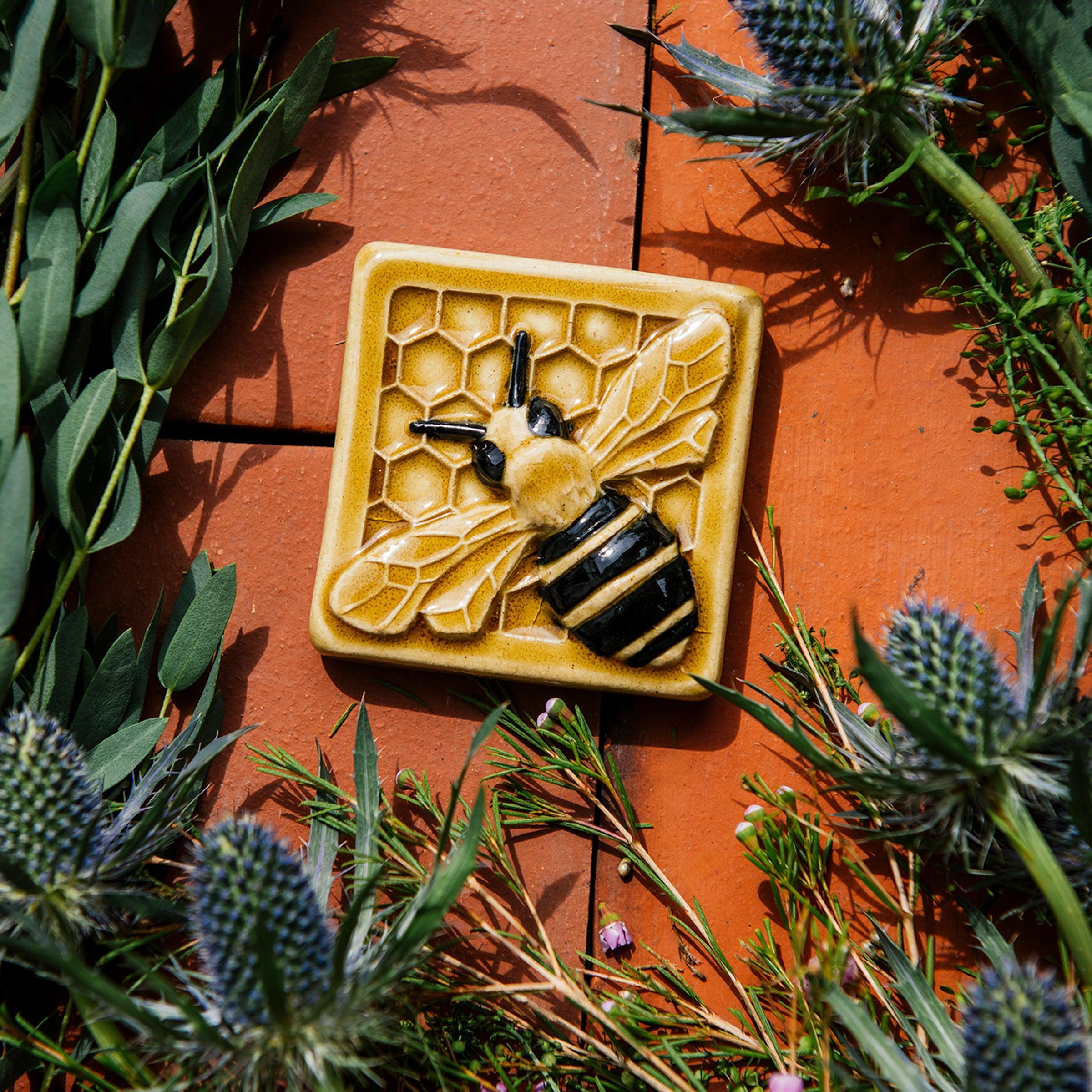 A glossy hand-painted Honeybee Tile in golden honey and black details surrounded by thistle. 