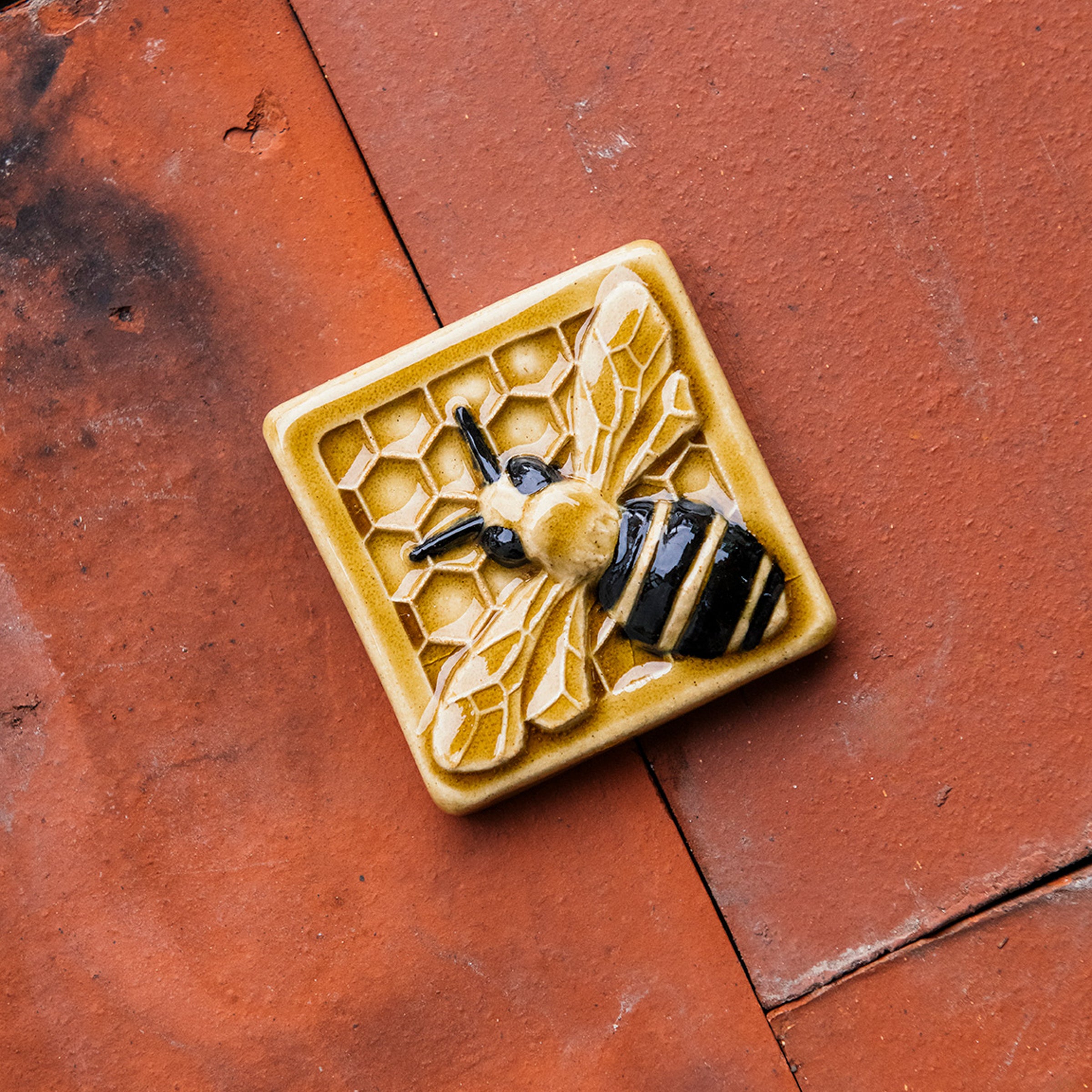 A glossy hand-painted Honeybee Tile in golden honey and black details. 