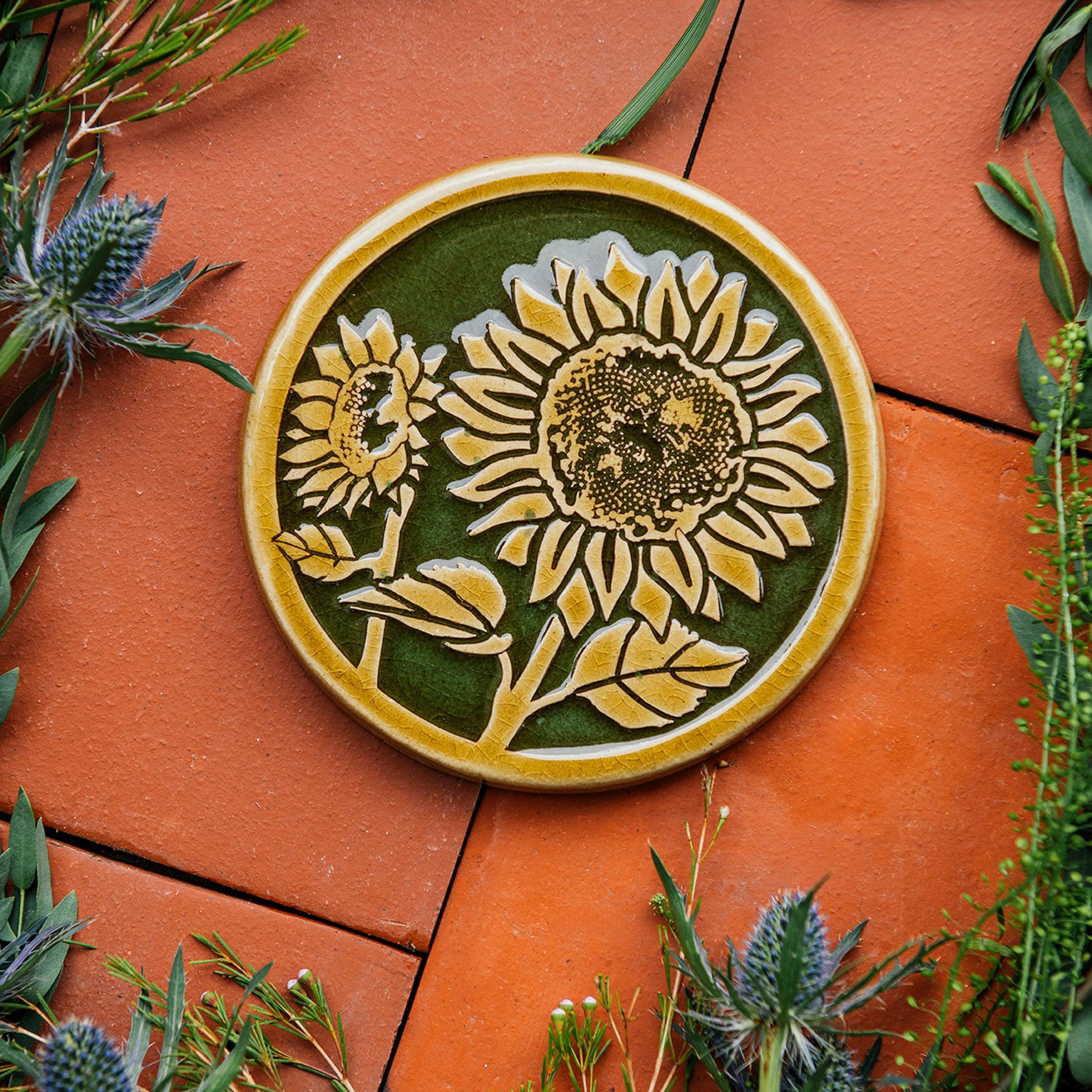 A two-tone glossy, round Sunflower Trivet with golden border and outline set against an emerald green background. 