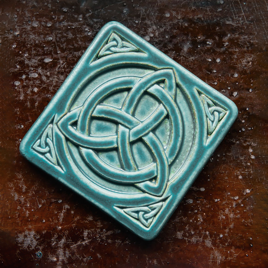 The Trinity Knot tile features a three-pointed Celtic knot interwoven with a circular ring. This knot is surrounded by a thick border with smaller three-pointed knots in each corner.