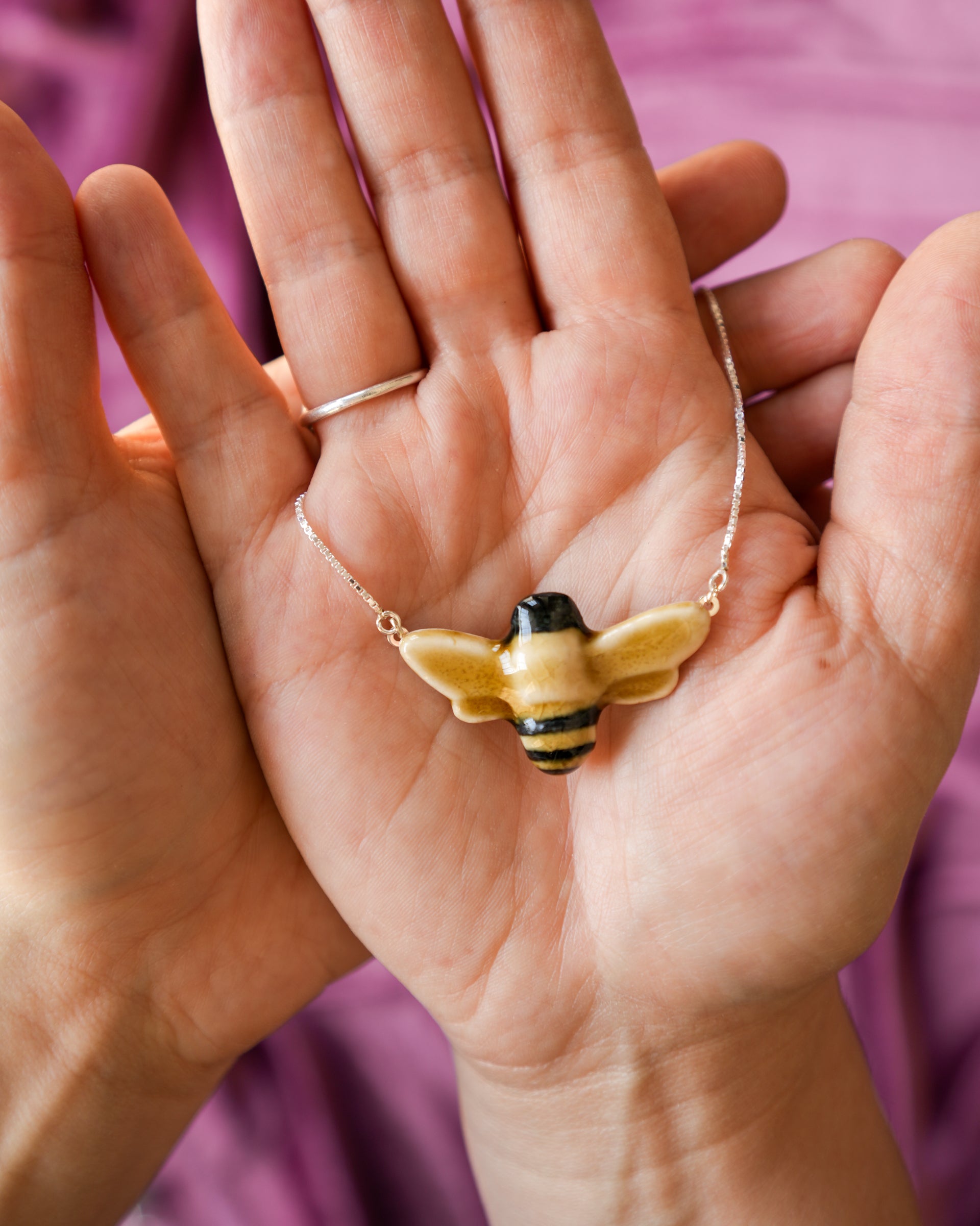 Hand holding a bee-shaped pendant necklace against a pink background