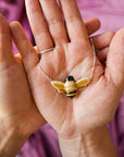 Hand holding a bee-shaped pendant necklace against a pink background