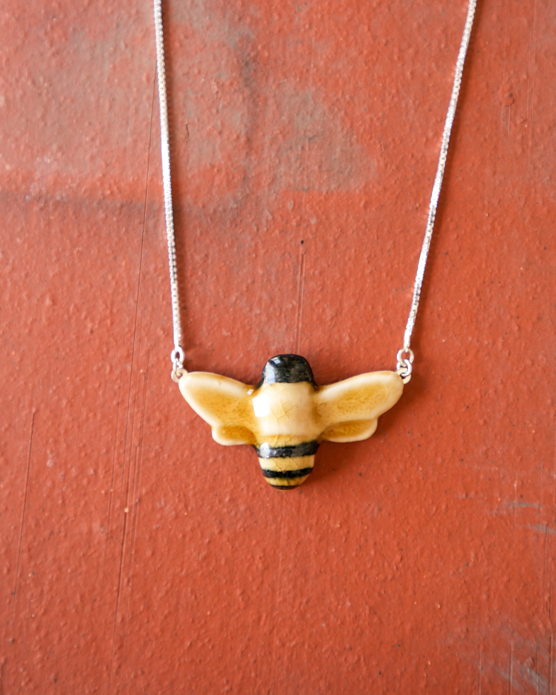 Glossy, hand-painted, bee-shaped pendant necklace on a red brick background