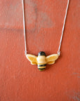 Glossy, hand-painted, bee-shaped pendant necklace on a red brick background