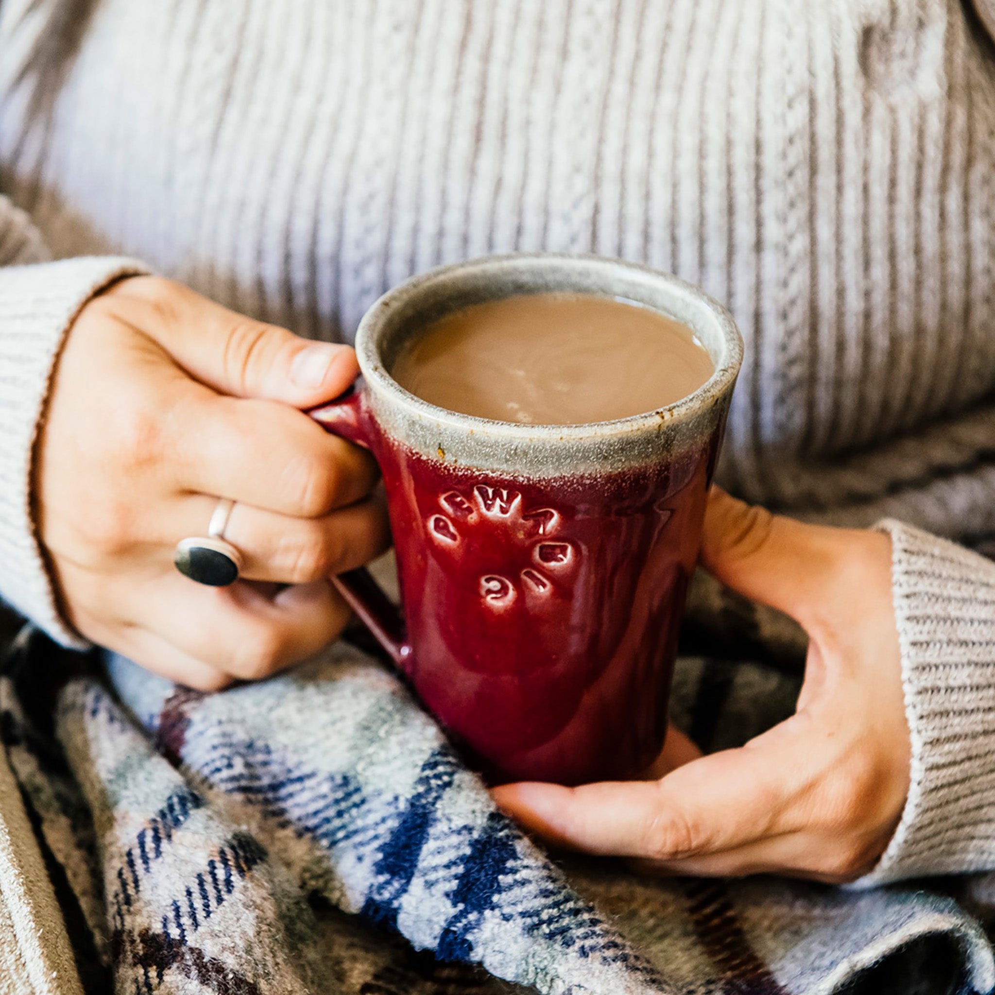 This Cafe Mug is being held by a woman in a cozy sweater with a blanket on her lap.