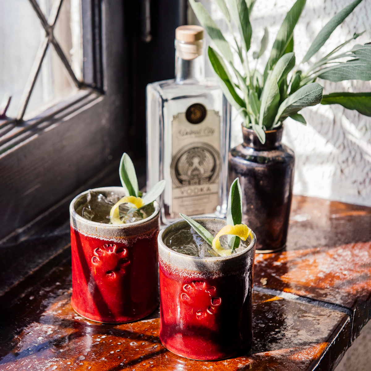 The Rocks Cups are short, cylindrical cups with smooth, straight sides. The Pewabic logo is stamped onto the side. There are two glazes featured on each cup - one is on the outside, covering the logo while the other glaze is on the inside of the cup and spills over creating a half inch ring around the outer lip of the cup. These cups feature the glossy, deep red Winterberry glaze on the outside and a gray glaze on the inside.