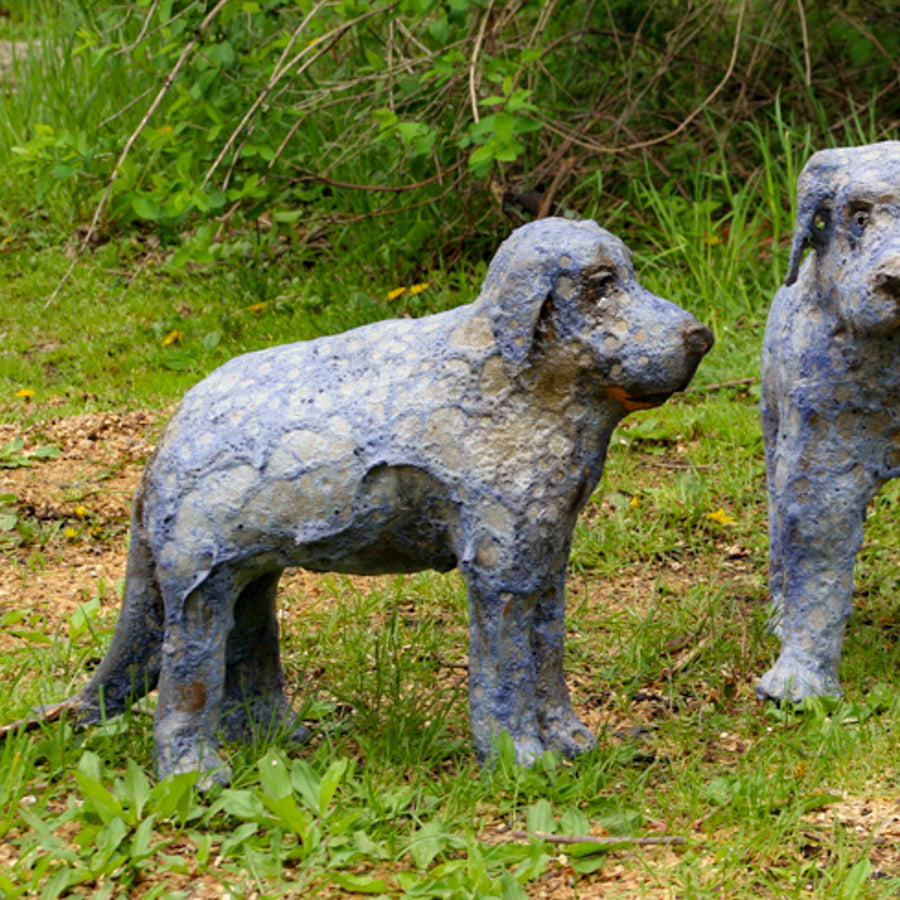 This cartoonish dog sculpture has wide eyes, floppy ears and a long tail. Its surface is extremely textured with a cobweb of steel blue covering its gray structure.