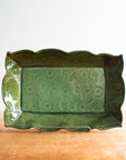 This rectangular dish has scalloped edges and a floral design- as if flowers and leaves were pressed into the surface of the clay. It is glazed in a glossy green color.