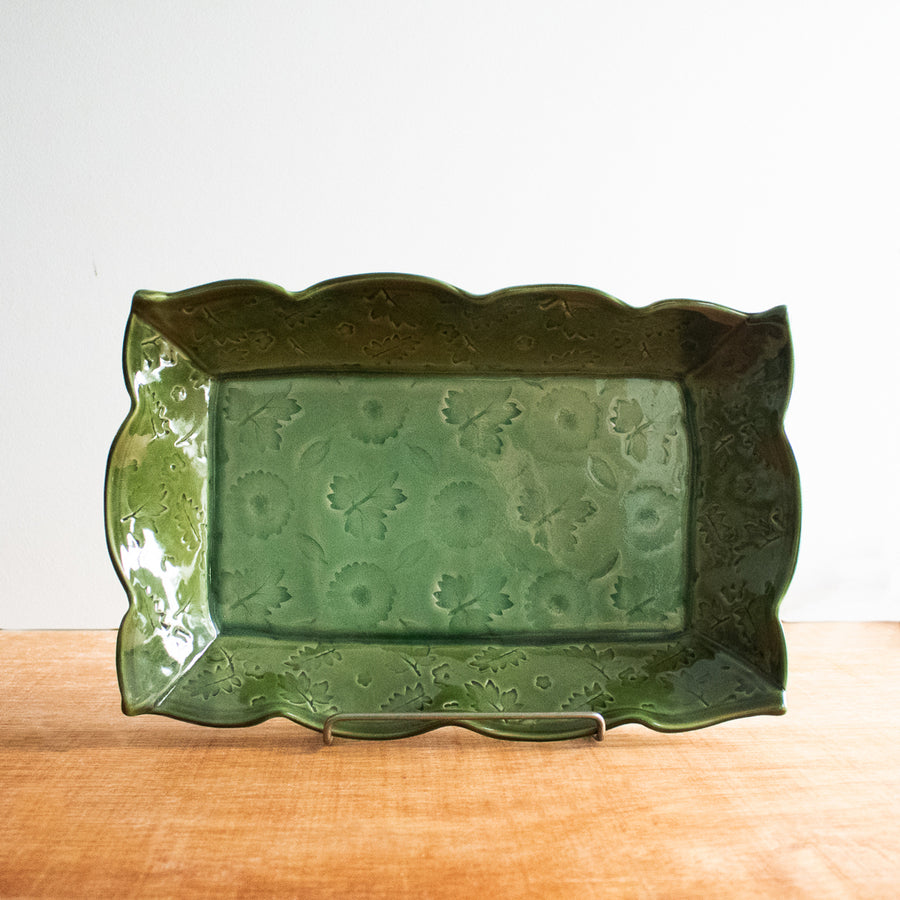 This rectangular dish has scalloped edges and a floral design- as if flowers and leaves were pressed into the surface of the clay. It is glazed in a glossy green color.