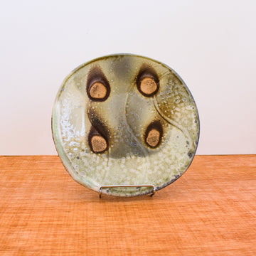 This Justin Lambert plate is many shades of organic gray colors. There are four circles where there is no glaze. This gives it the look of a button.