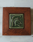 The Spartan Tile features a Spartan helmet with a large crest. This tile is in the glossy deep green Kale glaze which beautifully offsets the deep reddish brown oak wood frame.