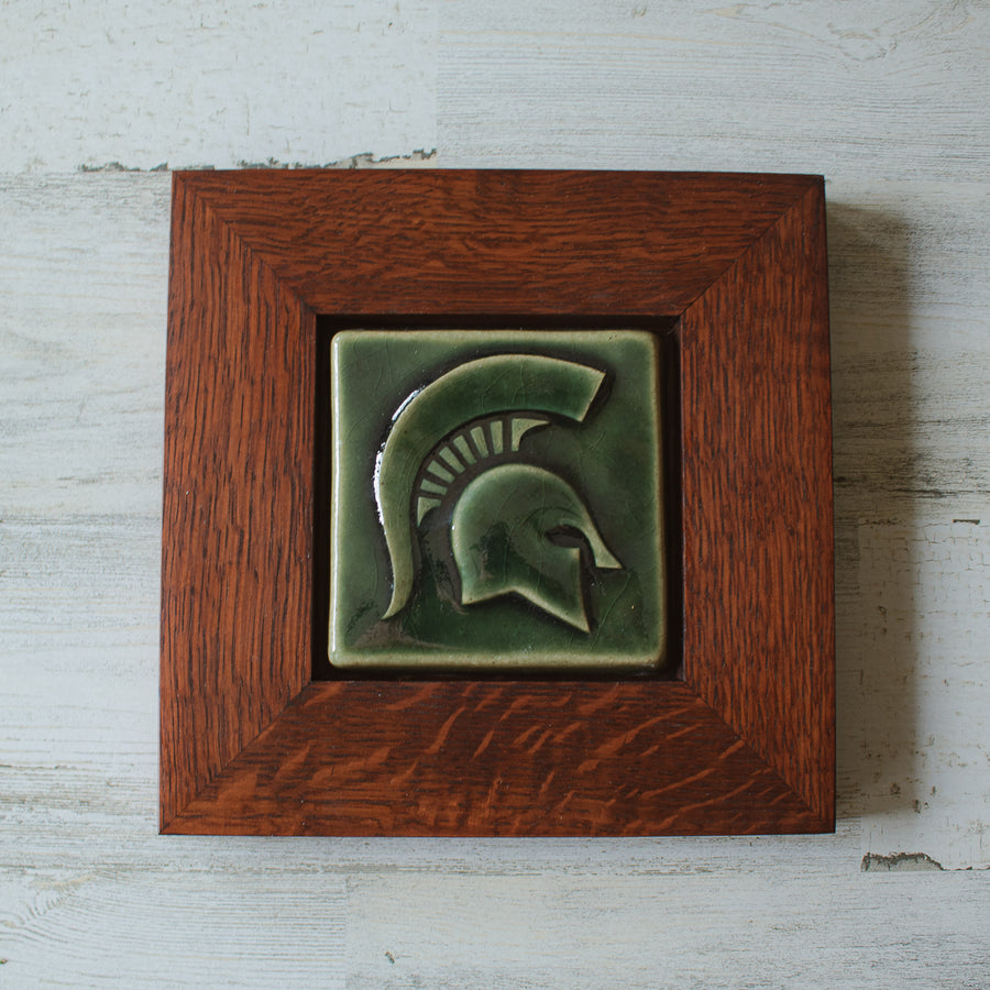 The Spartan Tile features a Spartan helmet with a large crest. This tile is in the glossy deep green Kale glaze which beautifully offsets the deep reddish brown oak wood frame.