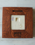 The back of the framed piece shows the open-back structure of the frame. This exposes the Pewabic Stamp one the back of the tile as well as the official sports licensing sticker. There is a burned on stamp of the woodworker who created the frame- it says "Handcrafted Family Woodworks".