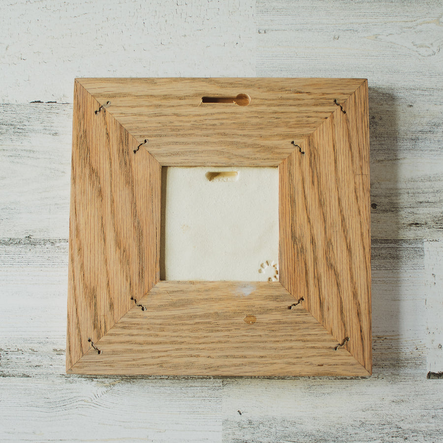 The back of the framed piece shows the open-back structure of the frame. This exposes the Pewabic Stamp one the back of the tile.