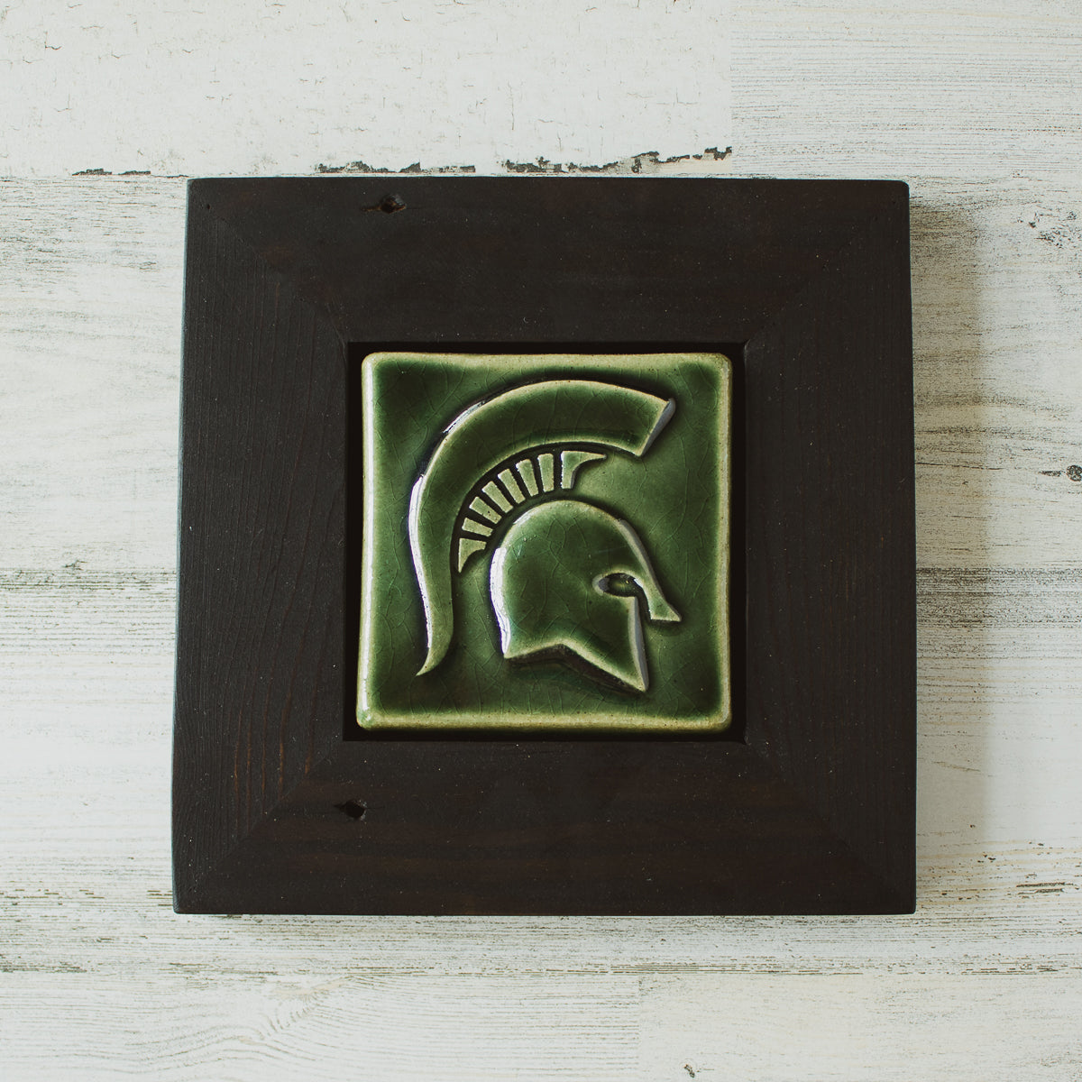 The Spartan Tile features a high relief design of a Spartan helmet with a large crest. This tile has the glossy deep green Kale glaze and sits in a black painted wood frame.