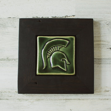 The Spartan Tile features a high relief design of a Spartan helmet with a large crest. This tile has the glossy deep green Kale glaze and sits in a black painted wood frame.