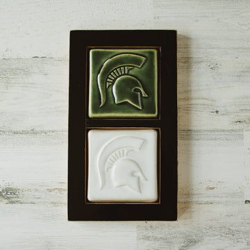 This black wooden framed piece features two Spartan tiles stacked on top of each other. Each tile has a high relief Spartan helmet design.. The top tile features the glossy deep green Kale glaze while the tile below has the satin finished white Alabaster glaze. 