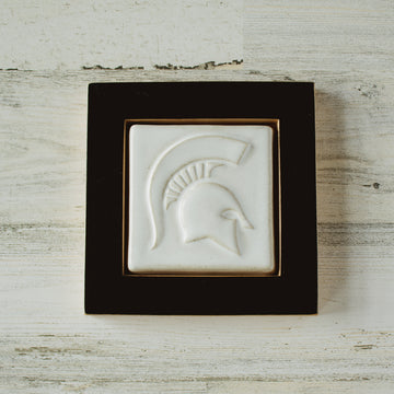 The Spartan Tile features a high relief design of a Spartan helmet with a large crest. This tile has the satin finished white Alabaster glaze and sits in a black painted wood frame.