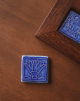 The glossy blue tile is flat on a wooden table next to a framed tile depicting a scarab.